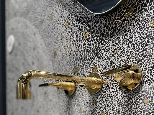 Gold faucet mounted on a wall with a black and white mosaic effect from Infinity Surfaces' Holus Collection.