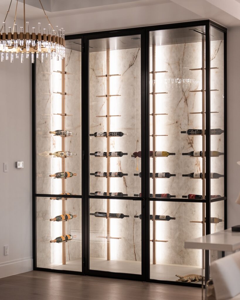 A modern wine wall featuring Neolith Crystallo Luz Effect sintered stone, a mineral surface that mimics the look of natural white marble with gray veining. The wine wall is illuminated, showcasing the material's elegance and highlighting its use as an alternative to natural stone.