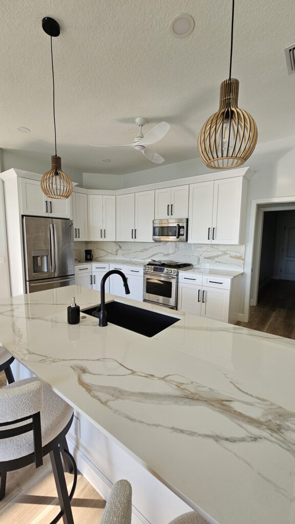 Seamless transition from kitchen countertop to full-height slab backsplash using polished Infinity Calacatta Oro 2cm porcelain.